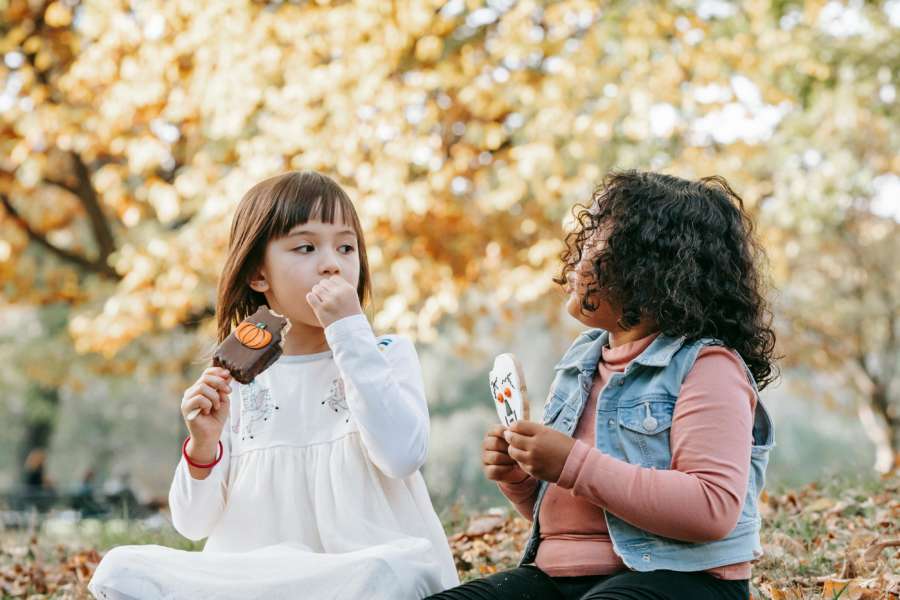 two kids sitting on a pile of leaves eating a treat