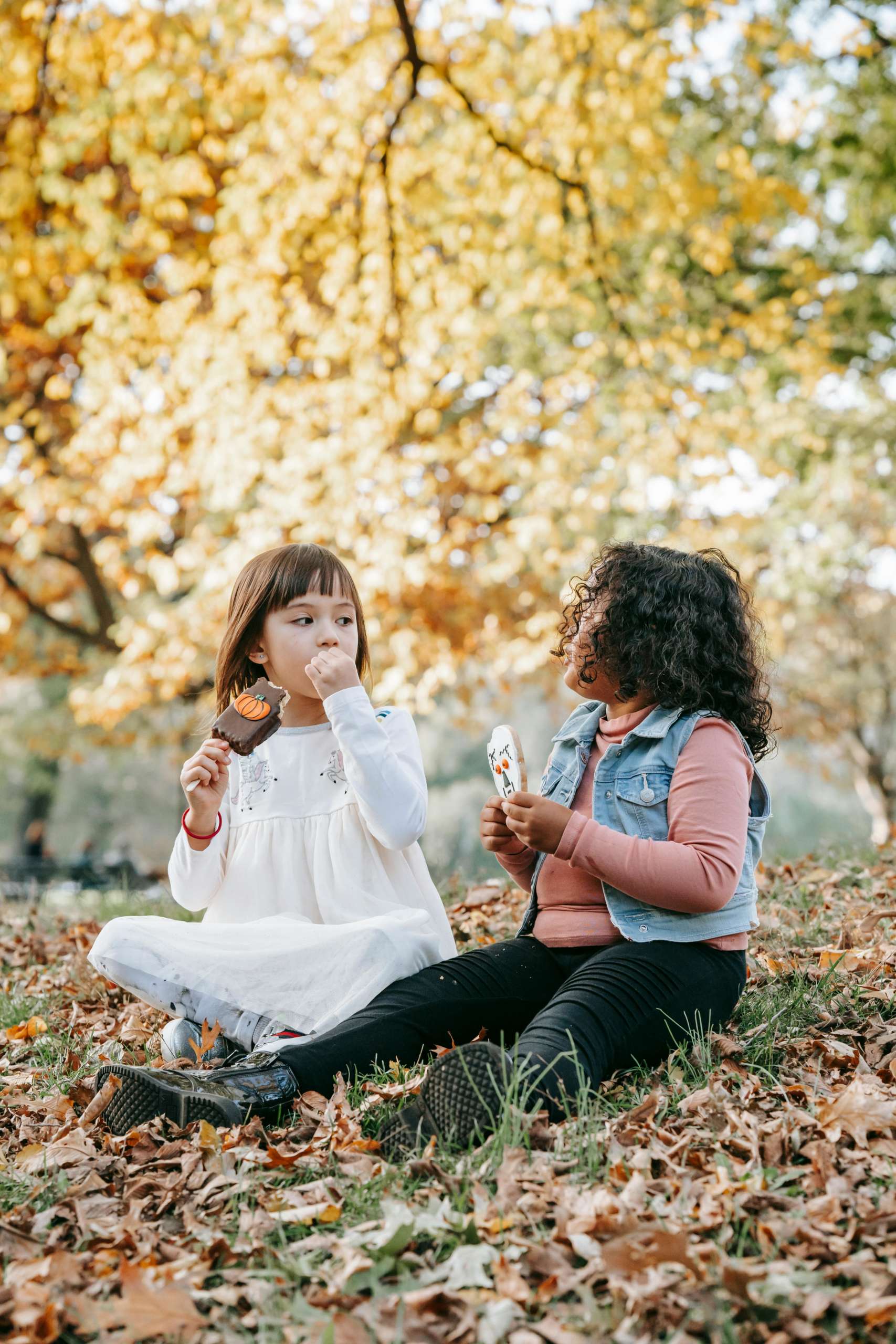 two kids sitting on a pile of leaves eating a treat